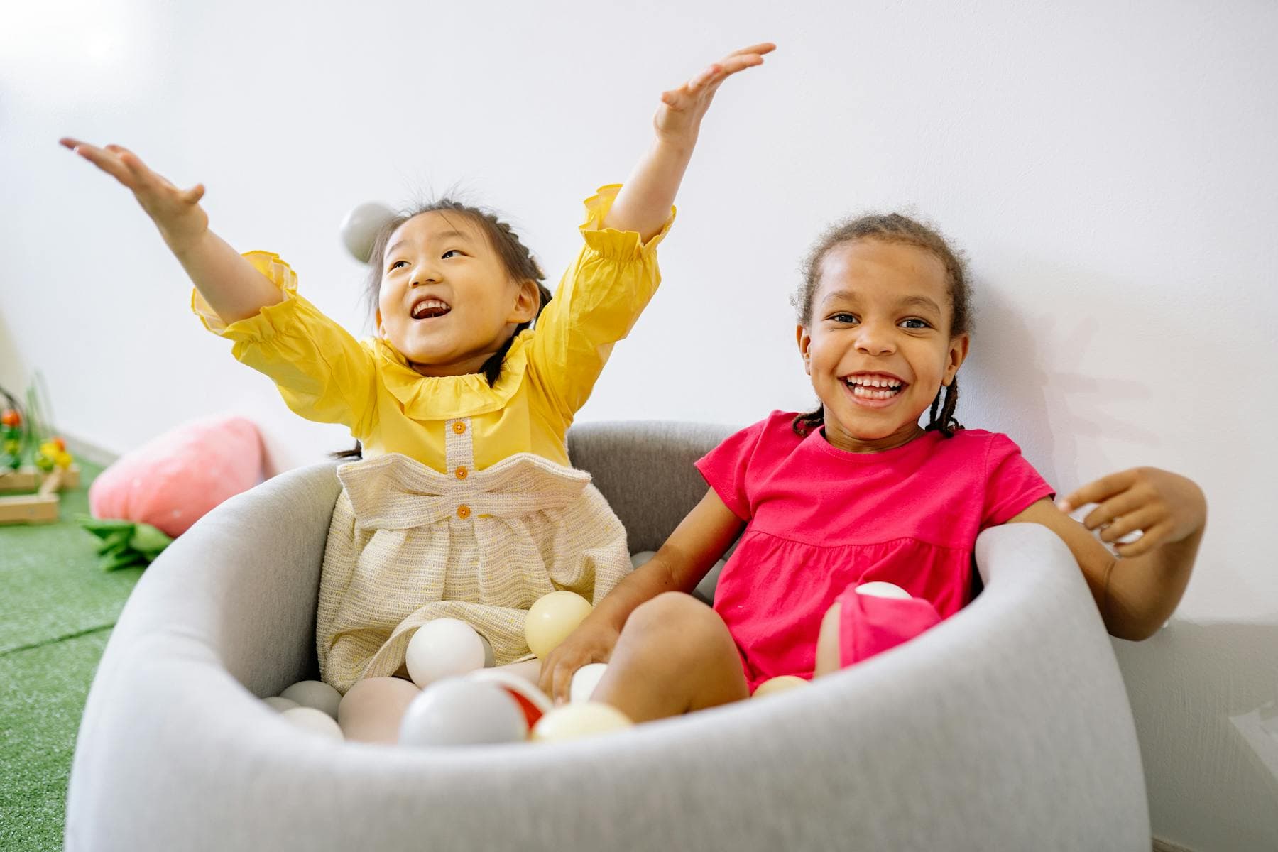 Two young children laugh and play together in a soft indoor ball pit.
