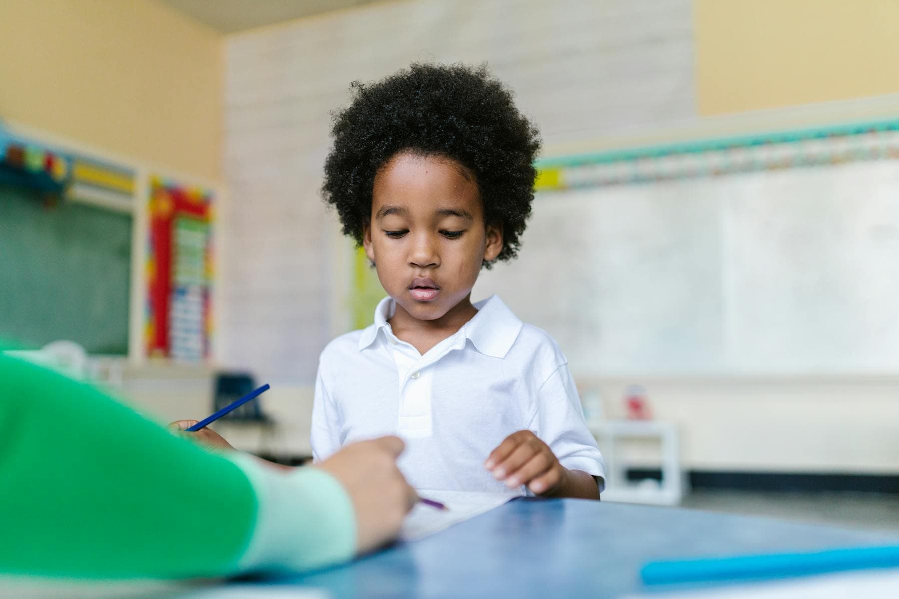 A young boy with an afro concentrates on his work at a classroom desk.
