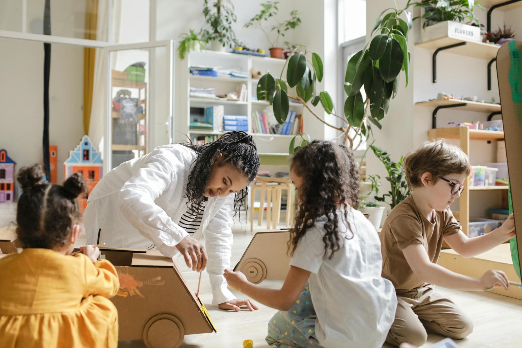 A teacher works with young children on a cardboard craft project in a bright classroom.