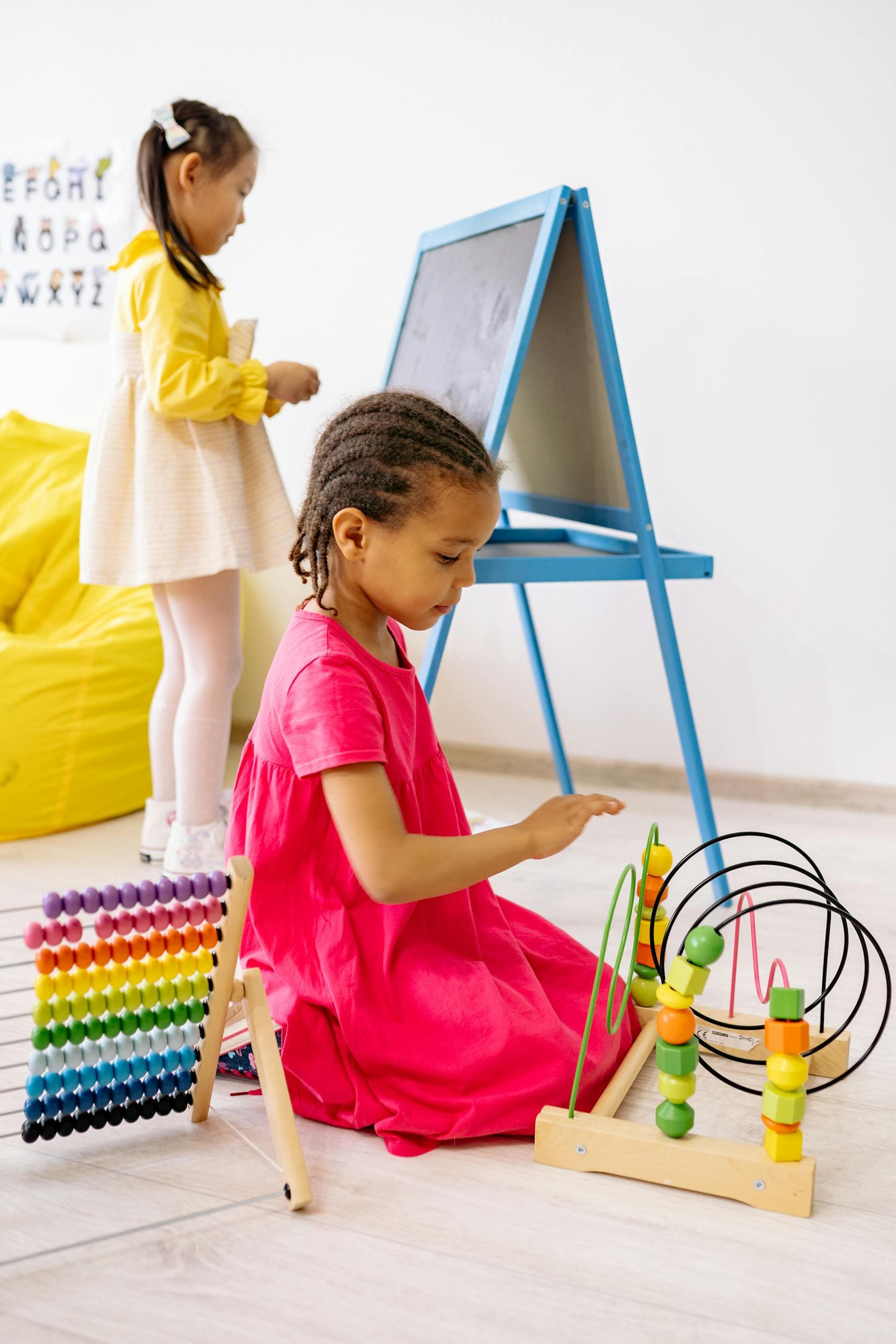 A young girl explores a colorful learning toy in a bright preschool room.
