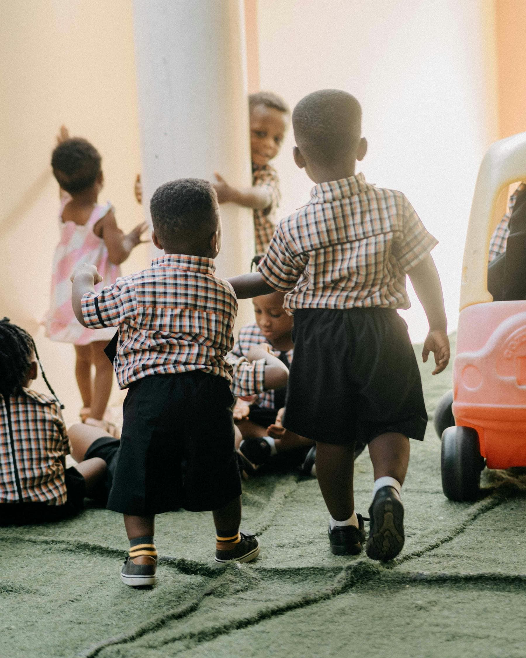 Toddlers in matching uniforms play and explore in a bright classroom.